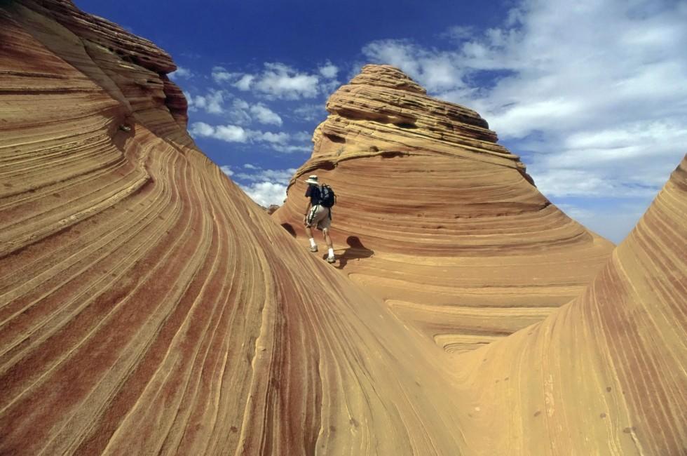 A lone hiker explores the astonishing candy stiped sandstone hidden amongst the geologic folds of the Colorado Plateau, Paria, Arizona