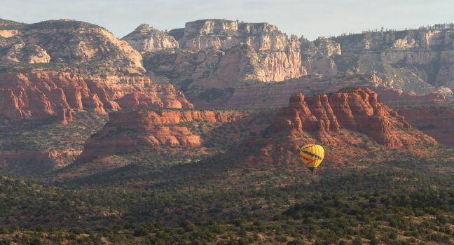 Aerial view of Sedona Arizona with a Hot air balloon soaring thru the red rock landscape.
