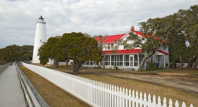White picket fence and walkway lead past the red-roofed keepers quarters towards the tower of the Ocracoke Island lighthouse on the outer banks of North Carolina