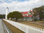 White picket fence and walkway lead past the red-roofed keepers quarters towards the tower of the Ocracoke Island lighthouse on the outer banks of North Carolina