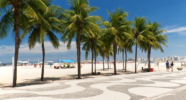 View of Copacabana beach with palms and mosaic of sidewalk in Rio de Janeiro. Brazil